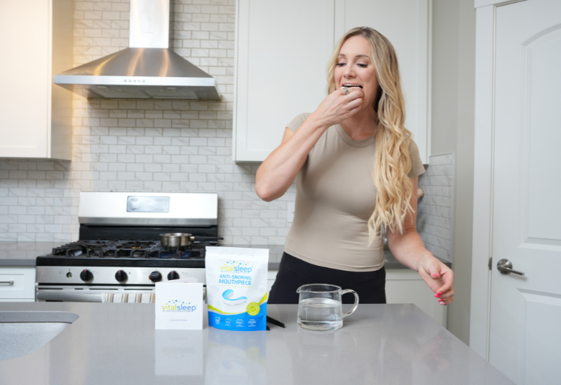 woman putting snoring device in mouth in kitchen after fitting