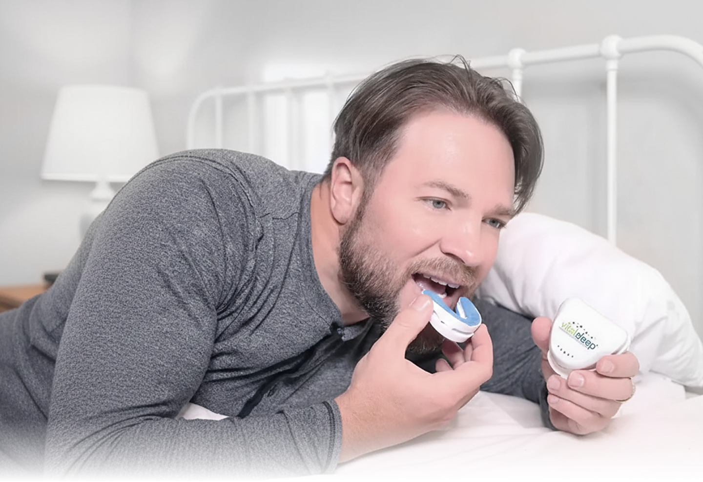 Man lying on a bed holding two bottles of a product, possibly a skincare or hygiene item.