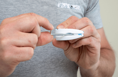 Person using a white handheld device, demonstrating functionality with hands, against a neutral background